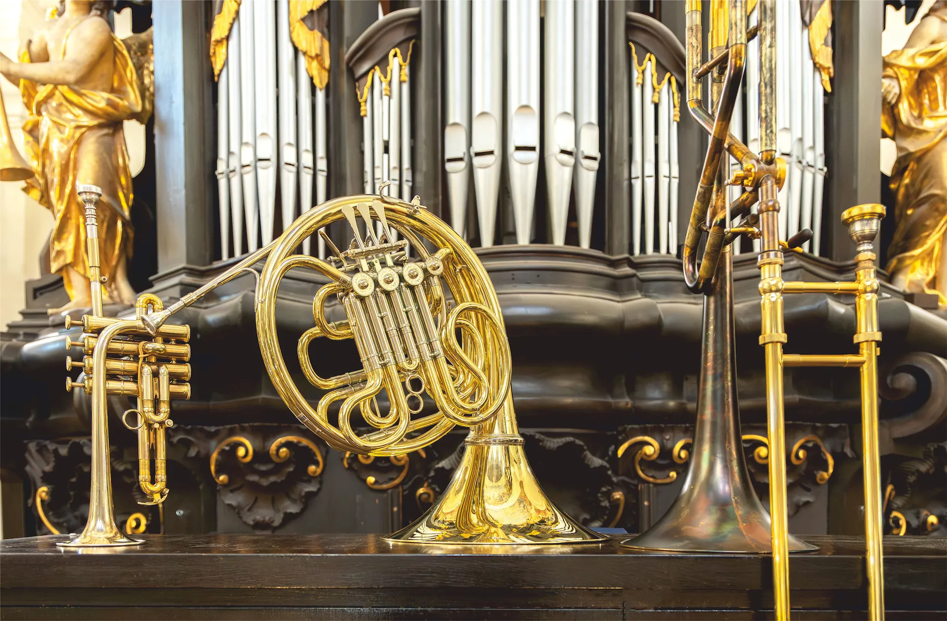Polished brass instruments displayed in front of the pipe organ at Kostel sv. Mikuláše